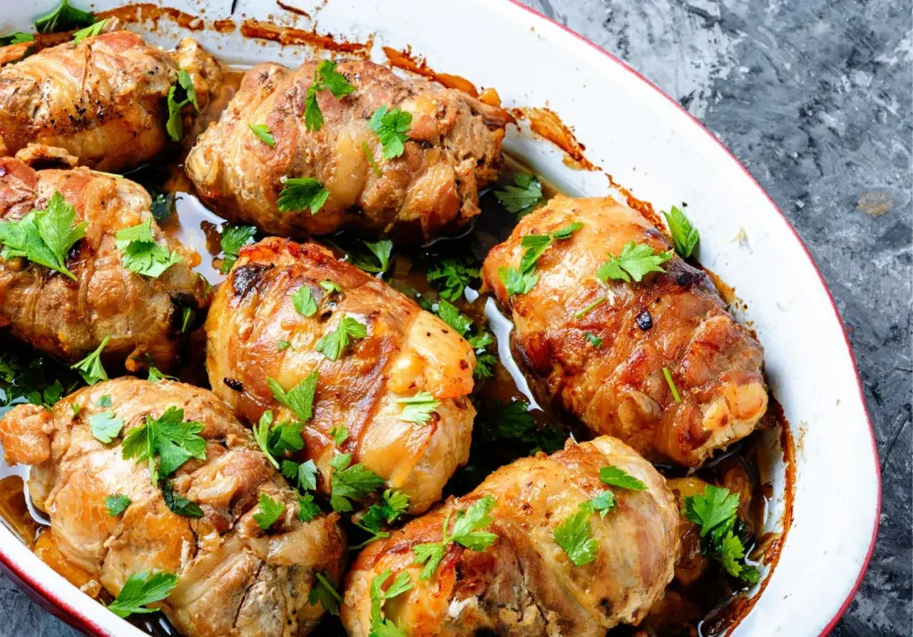 Involtini di carne dorati e succulenti, guarniti con prezzemolo fresco, cotti in una teglia bianca con bordo rosso.