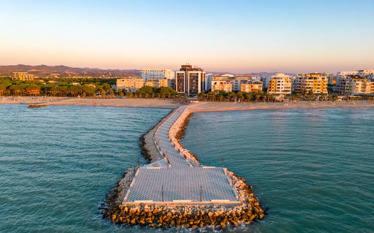 Promenada na plaży w Durrës, z budynkami w tle i spokojnym morzem.