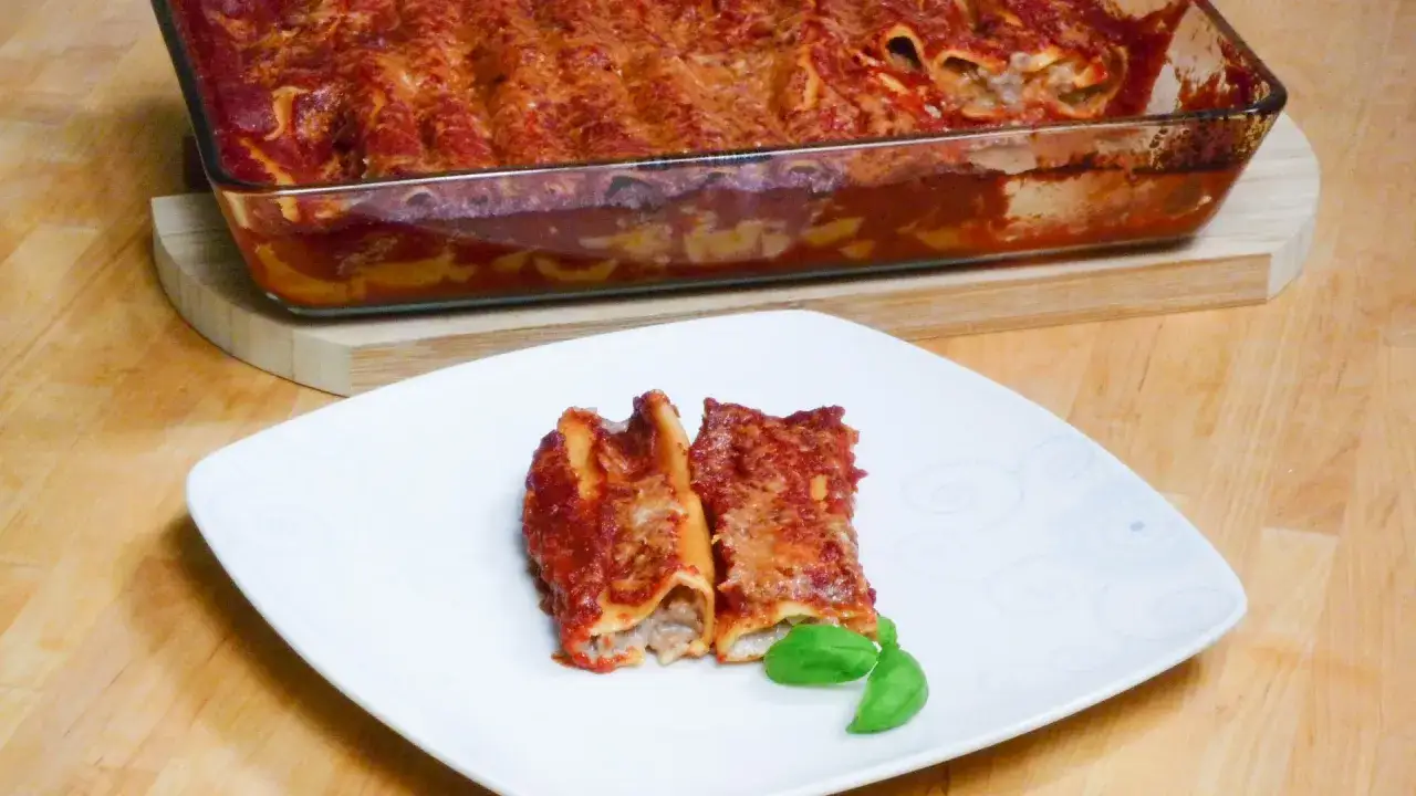 Zwei Cannelloni auf einem Teller, daneben eine Auflaufform mit vielen gef&uuml;llten Nudeln in Tomatenso&szlig;e. Ein k&ouml;stliches Cannelloni Rezept!