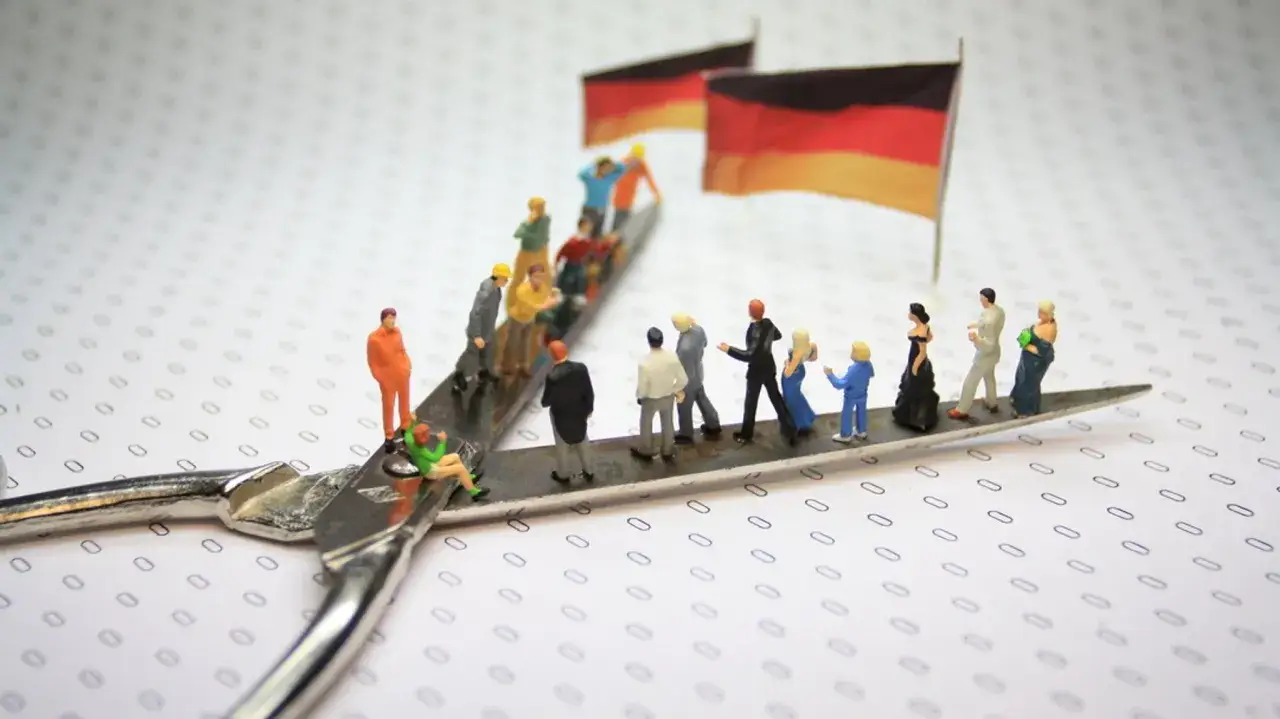 Miniaturfiguren auf einer Schere, die deutsche Flaggen und verschiedene **Soziologie Themen** wie Migration und soziale Schichten darstellen.