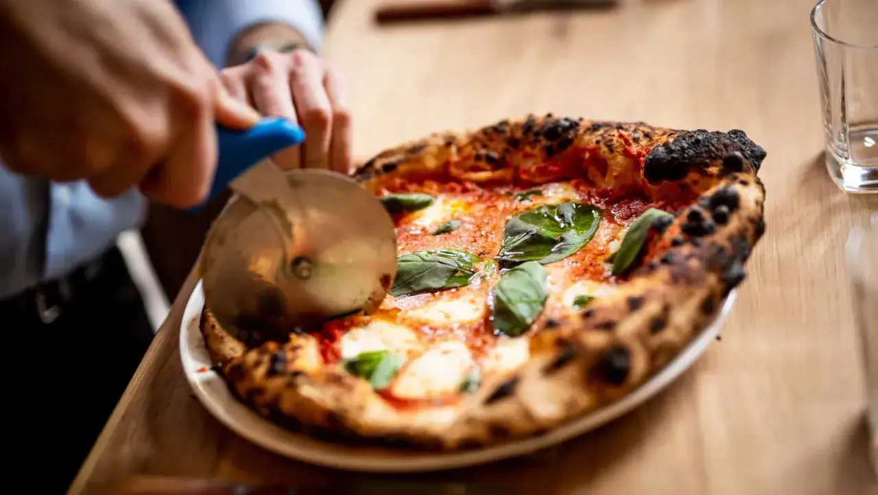 Ręce kroją pyszną pizzę Margherita. Zastanawiasz się, ile kosztuje pizza w Czechach? Ta wygląda na wartą swojej ceny!