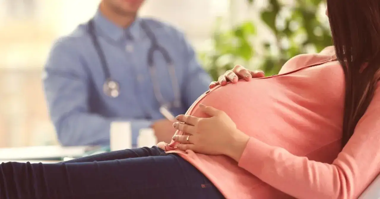 Kobieta w wieku 47 lat, po in vitro, czule dotyka swojego ciążowego brzucha podczas wizyty u lekarza.