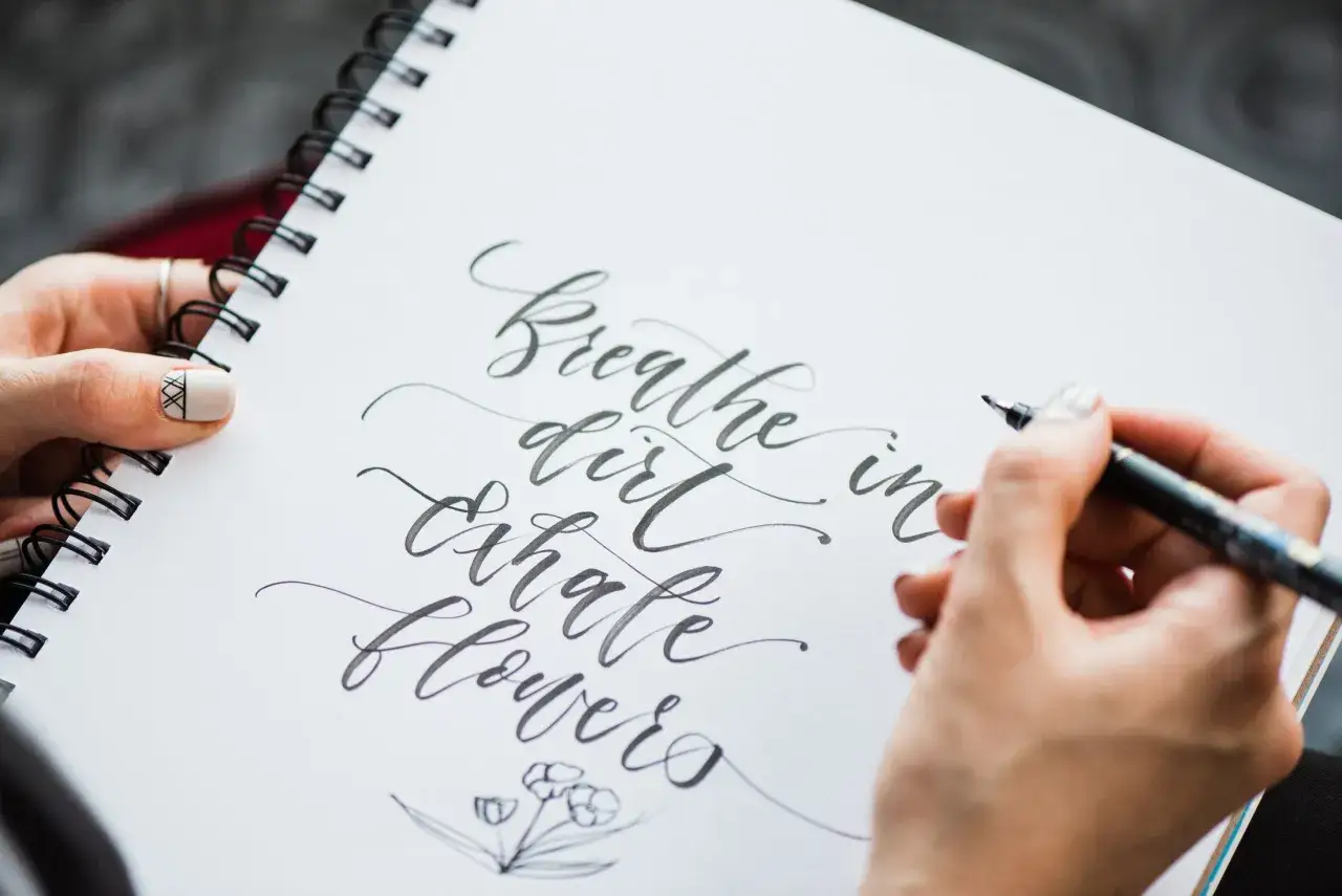 Manos practicando lettering en un cuaderno. 