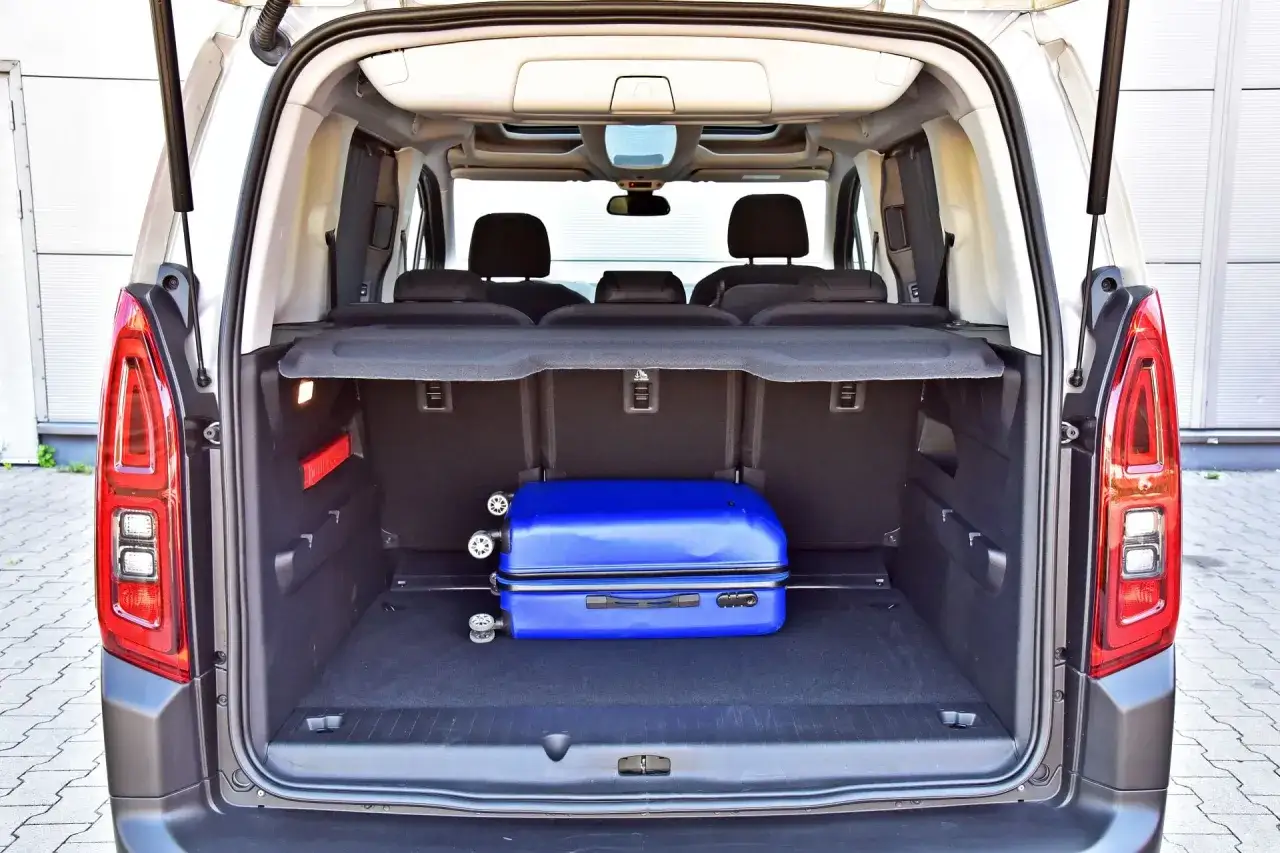 Bagażnik Citroëna Berlingo gotowy na podróż. W środku znajduje się niebieska walizka, a za nią widać złożone siedzenia.