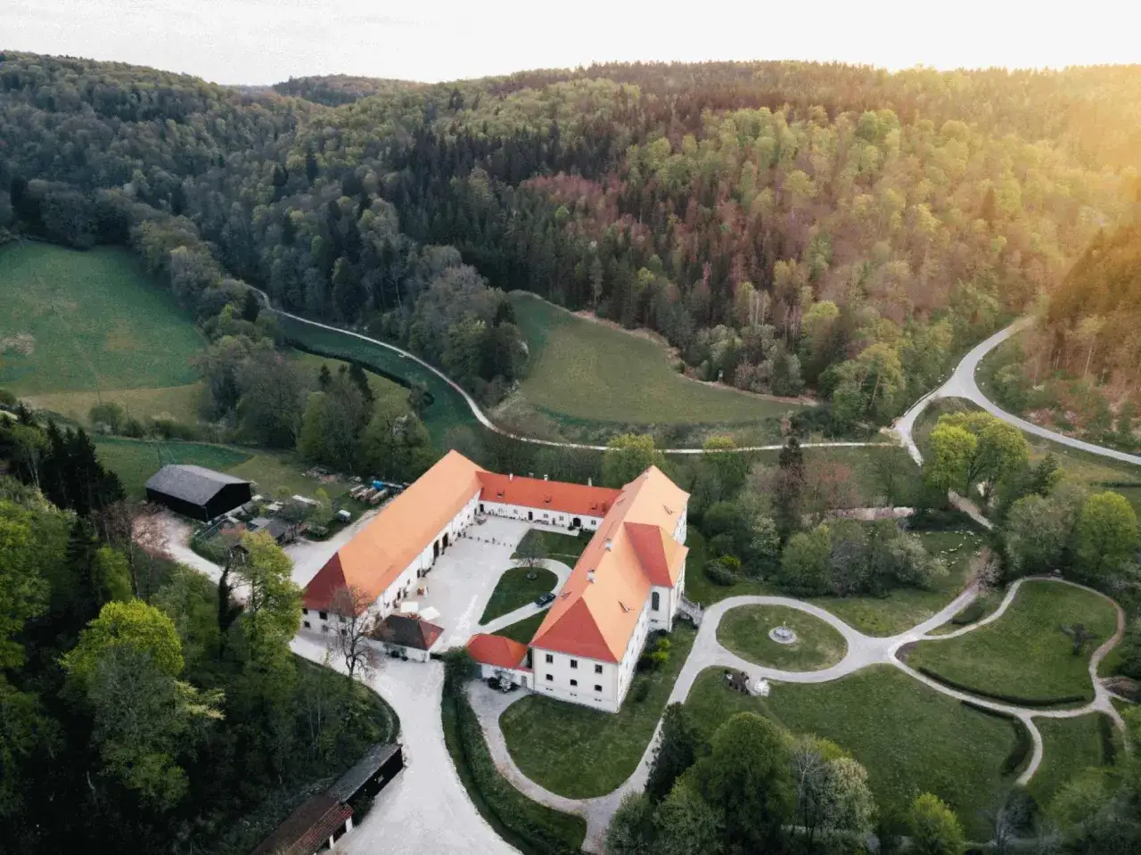 Schloss Ehrenfels bei Hayingen, ein weitl&auml;ufiger Geb&auml;udekomplex mit roten D&auml;chern, eingebettet in eine gr&uuml;ne H&uuml;gellandschaft mit W&auml;ldern und Wiesen.