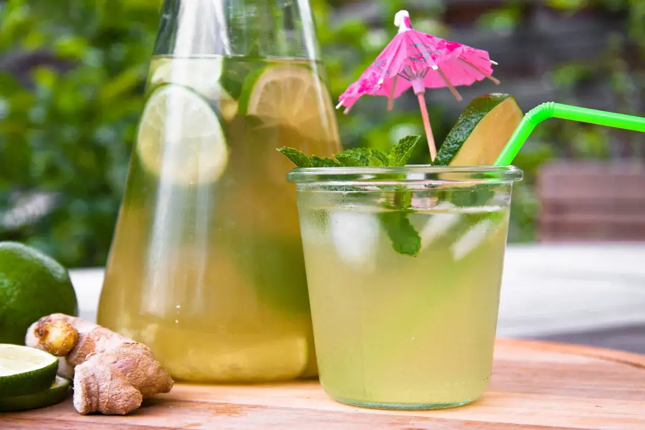 Une carafe et un verre remplis de thé glacé rafraîchissant avec des tranches de citron vert, de la menthe et du gingembre. Parfait pour une recette de thé glacé maison.