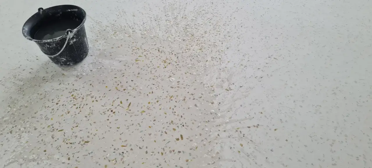 Un seau d'eau éclabousse un sol en terrazzo blanc, révélant comment faire briller un sol en terrazzo.
