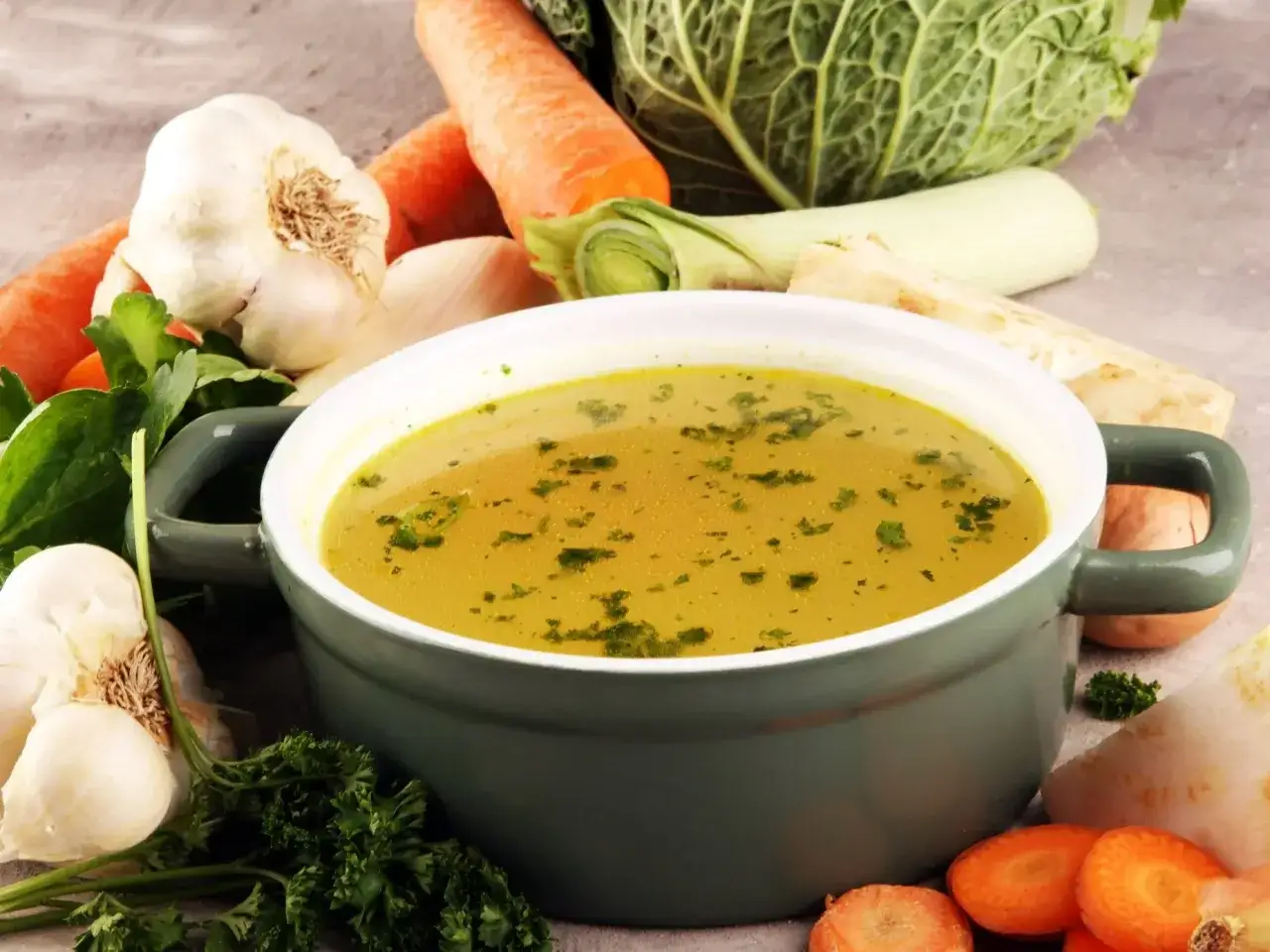 Aromaticzny bulion w garnku, otoczony warzywami: marchewką, kapustą, czosnkiem i pietruszką. Idealny przepis, jak zrobić bulion.