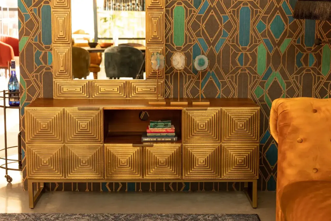 Złota komoda i lustro w stylu art deco w Polsce. Geometryczna tapeta i aksamitny fotel dopełniają eleganckie wnętrze.