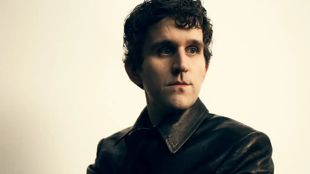 Harry Melling w skórzanej kurtce, znany z filmów, seriali i programów, patrzy w bok.
