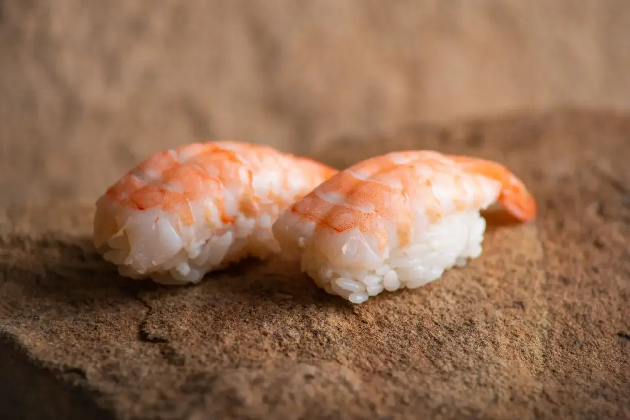 Dwa kawałki sushi z krewetkami na kamiennym podłożu. Idealne, gdy zastanawiasz się, jak przygotować krewetki do sushi.