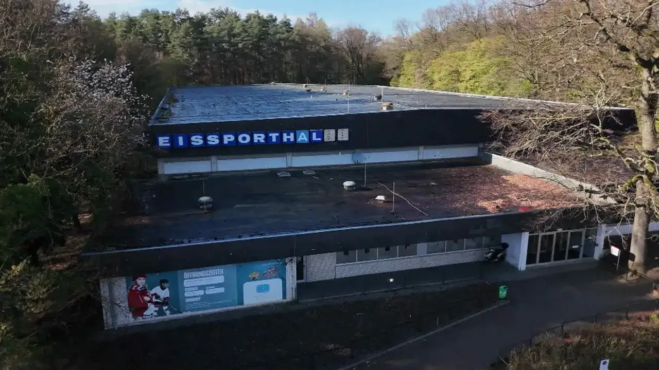 Die Eissporthalle Bergisch Gladbach, umgeben von B&auml;umen, mit leuchtenden Buchstaben am Dach.