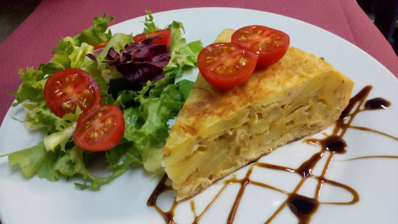 Un trozo de tortilla de patatas con tomates cherry y ensalada verde, decorado con reducci&oacute;n de bals&aacute;mico.