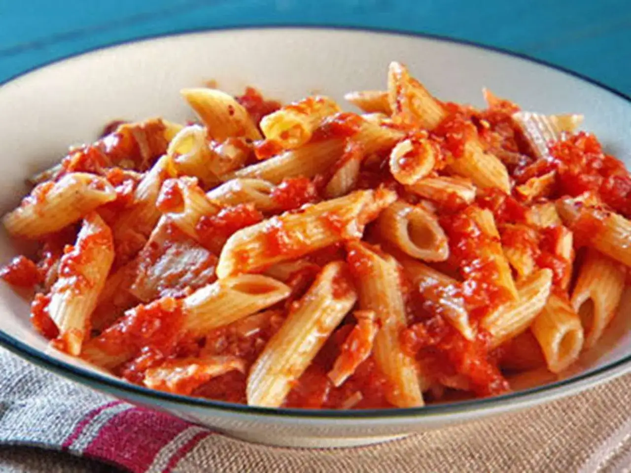 Eine Schüssel Penne mit einer herzhaften Tomatensoße, die Stücke von Thunfisch enthält.