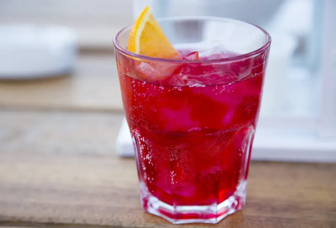 Ein erfrischender Sloe Gin Fizz mit Eis und einer Orangenspalte, sprudelnd und leuchtend rot.