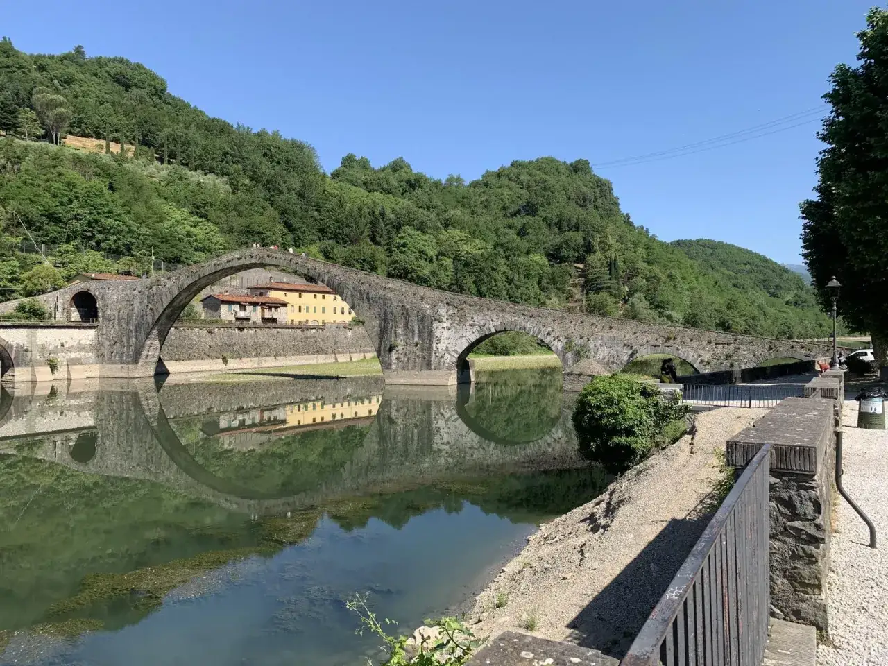 Ponte del Diavolo a Borgo a Mozzano, con le sue arcate che si specchiano nel fiume Serchio, circondato da colline verdi.