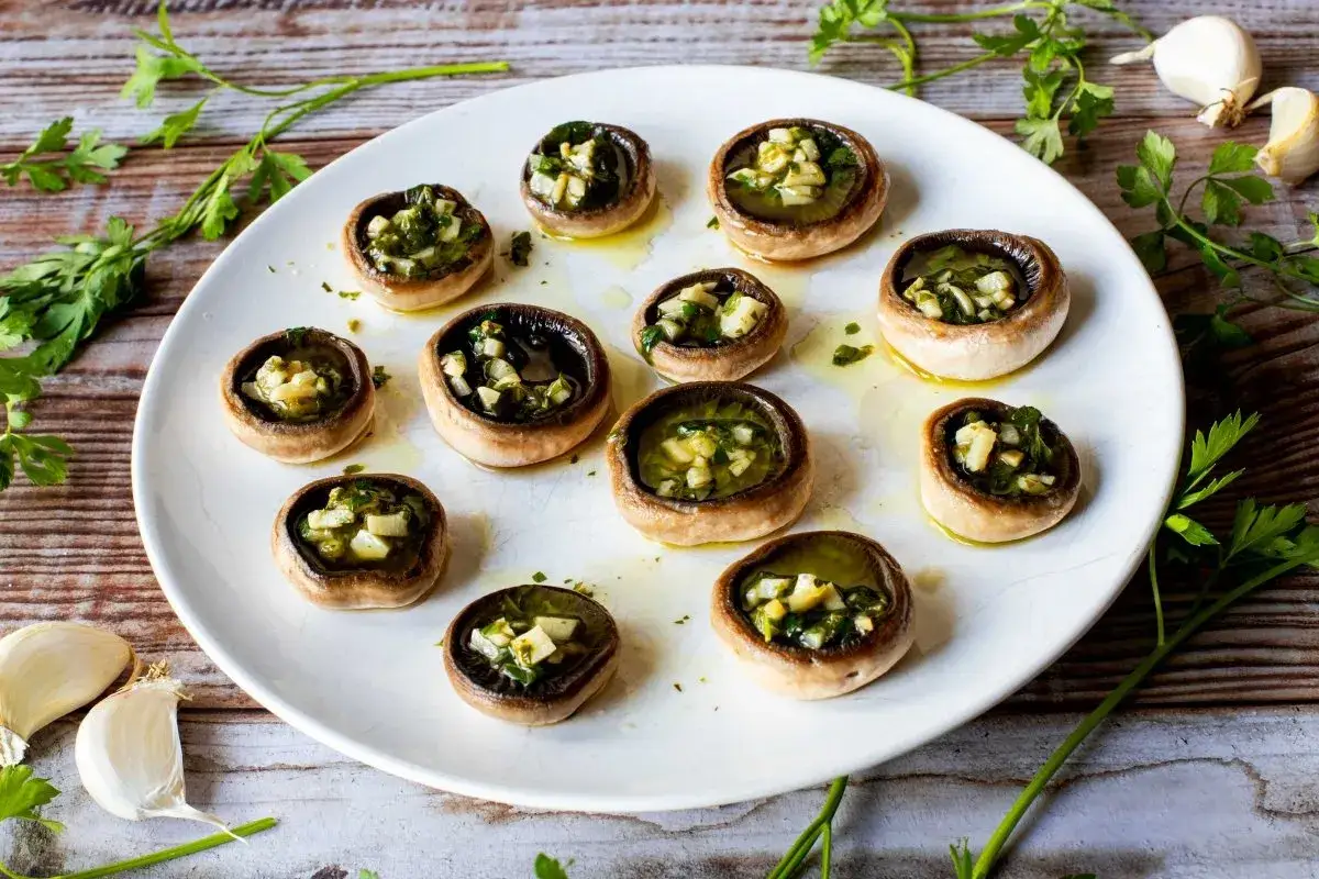Champiñones a la plancha rellenos de ajo y perejil, servidos en un plato blanco sobre una mesa de madera.
