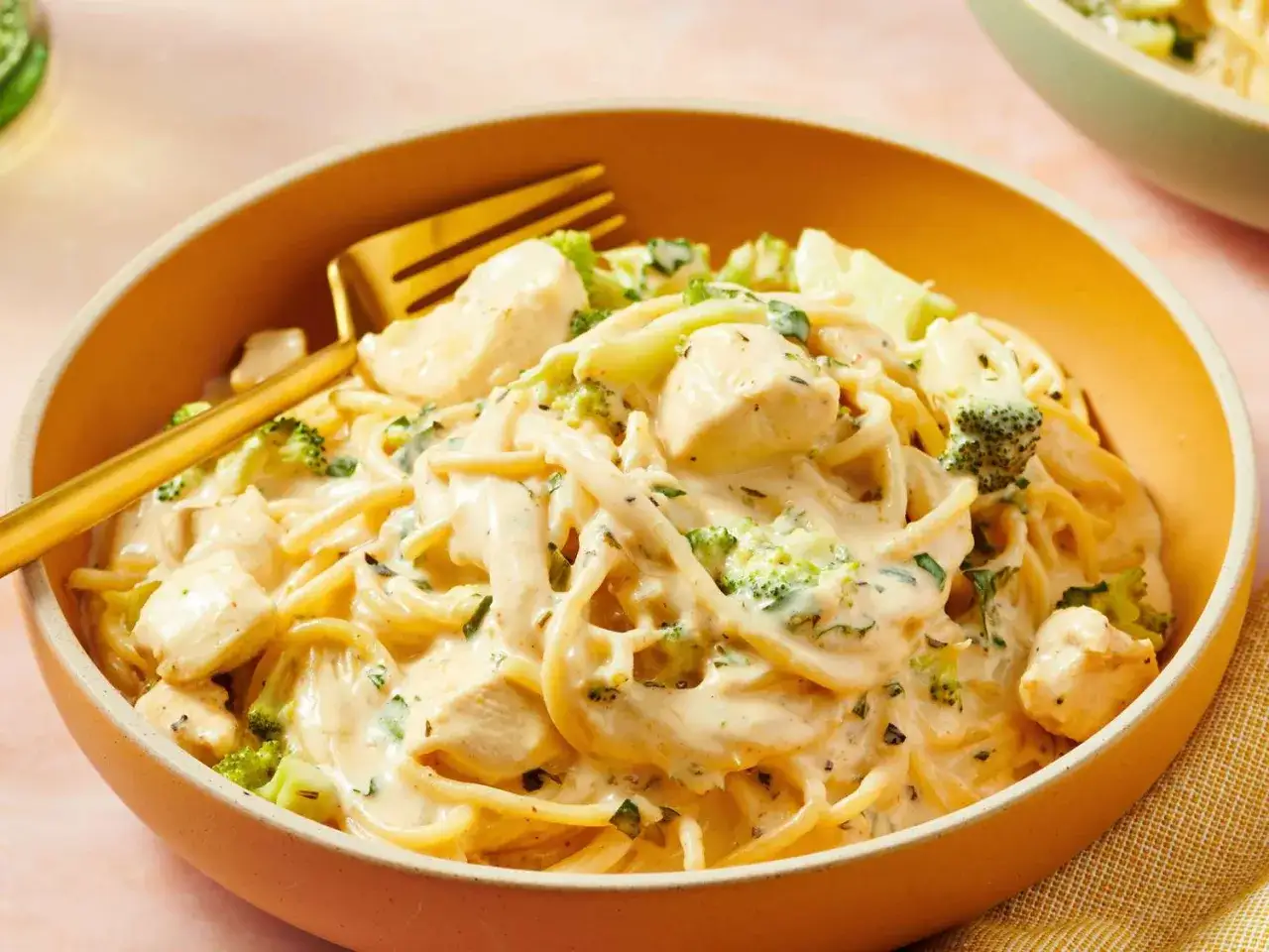 Cremiges Chicken Alfredo mit zarten H&auml;hnchenst&uuml;cken und knackigem Brokkoli, serviert in einer Sch&uuml;ssel mit goldenem Besteck.