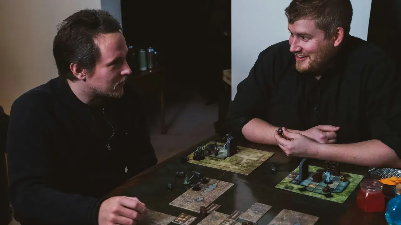 Zwei Freunde spielen ein episches Abenteuer. Sie sind vertieft in eines der besten 2 Spieler Brettspiele, mit Miniaturen und Würfeln auf dem Tisch.