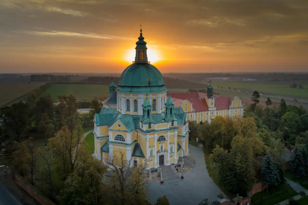 Zach&oacute;d słońca nad barokową bazyliką. Złote światło oświetla ż&oacute;łte mury i zielone kopuły, tworząc magiczną atmosferę na świętej g&oacute;rze.