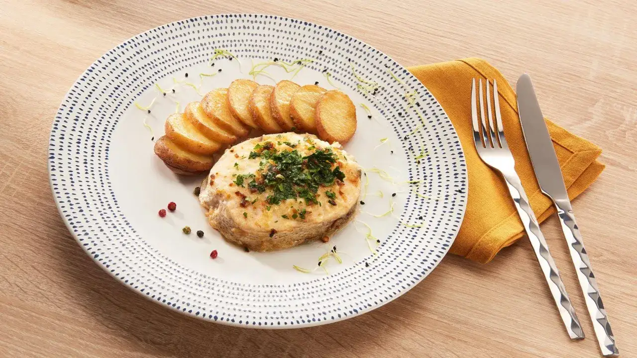 Merlu poêlé, doré et garni de persil, servi avec des rondelles de pommes de terre. Le temps cuisson merlu poêle est parfait pour ce plat.