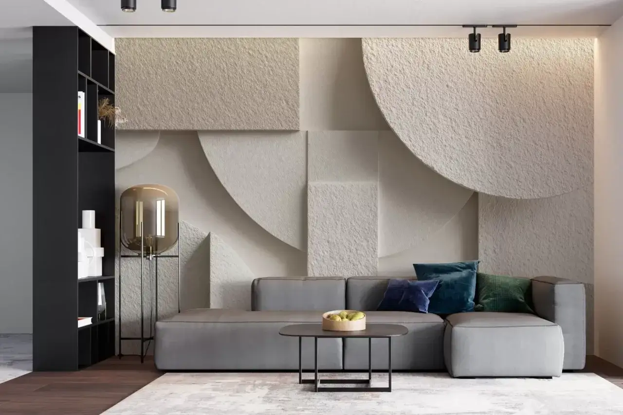 Un sal&oacute;n moderno con sof&aacute; gris, mesa de centro y estanter&iacute;a negra. La pared tiene un relieve abstracto que inspira a aprender a pintar.