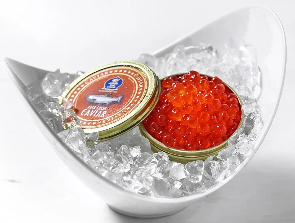 Roter Kaviar, Keta-Lachs-Kaviar, präsentiert in einer Eisschale. Die Dose zeigt einen Fisch, der auf den Ursprung des Kaviars hinweist.