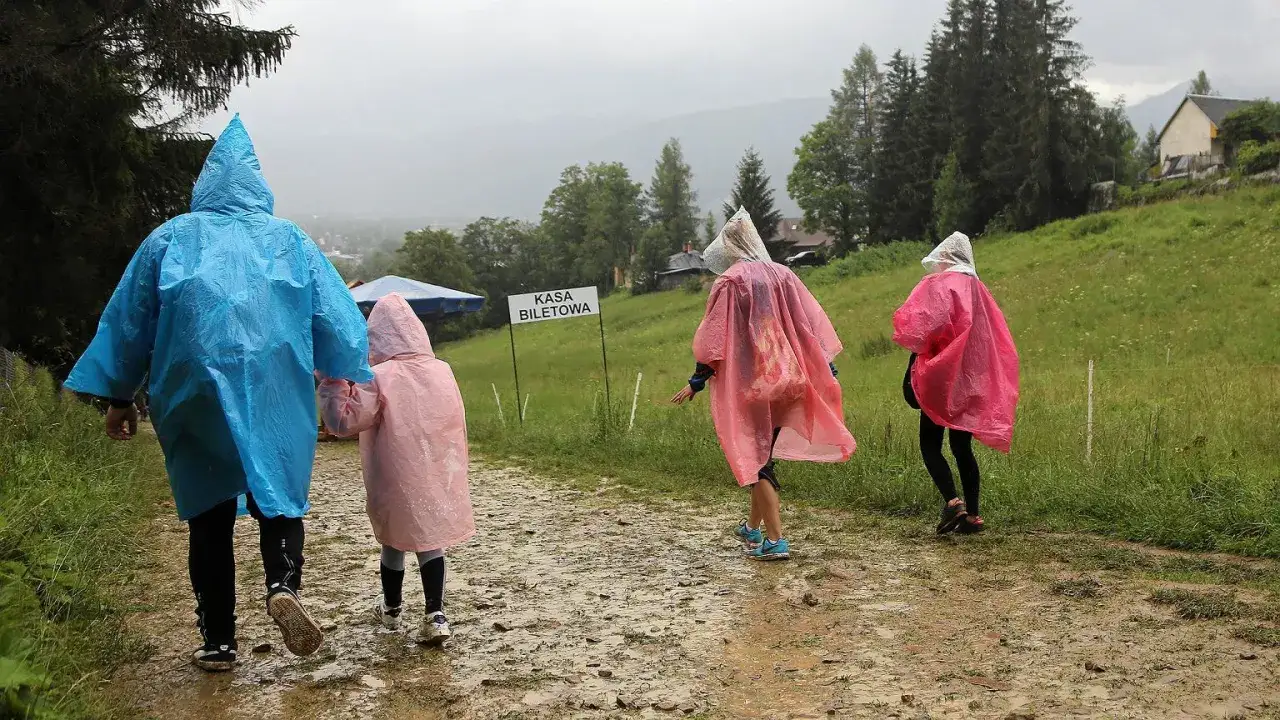 Rodzina w kolorowych pelerynach idzie błotnistą ścieżką. Nawet gdy pada deszcz, w Zakopanem można znaleźć ciekawe atrakcje.