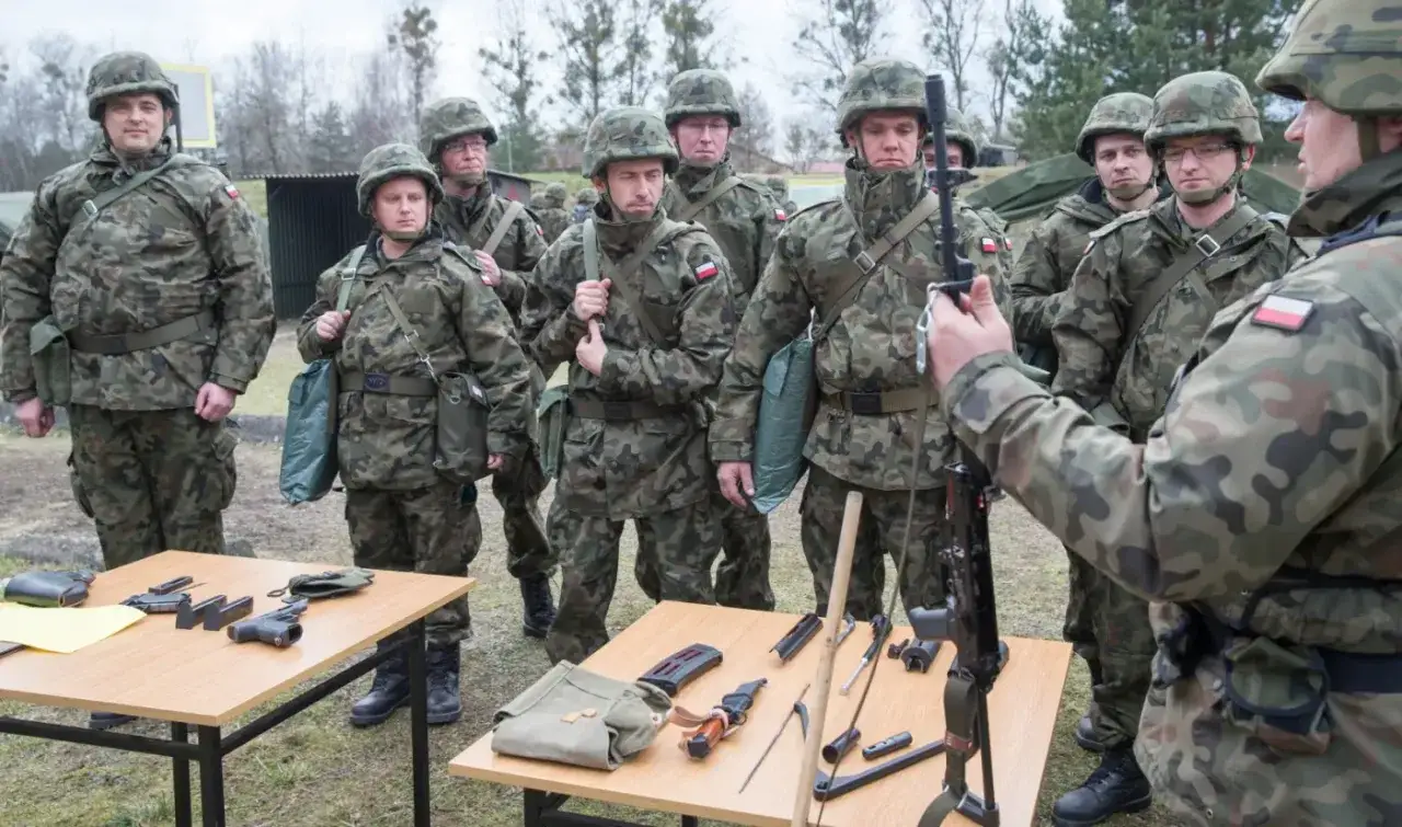 Żołnierze w mundurach ćwiczą, przygotowując się do mobilizacji w Polsce. Na stole leżą pistolety i magazynki.