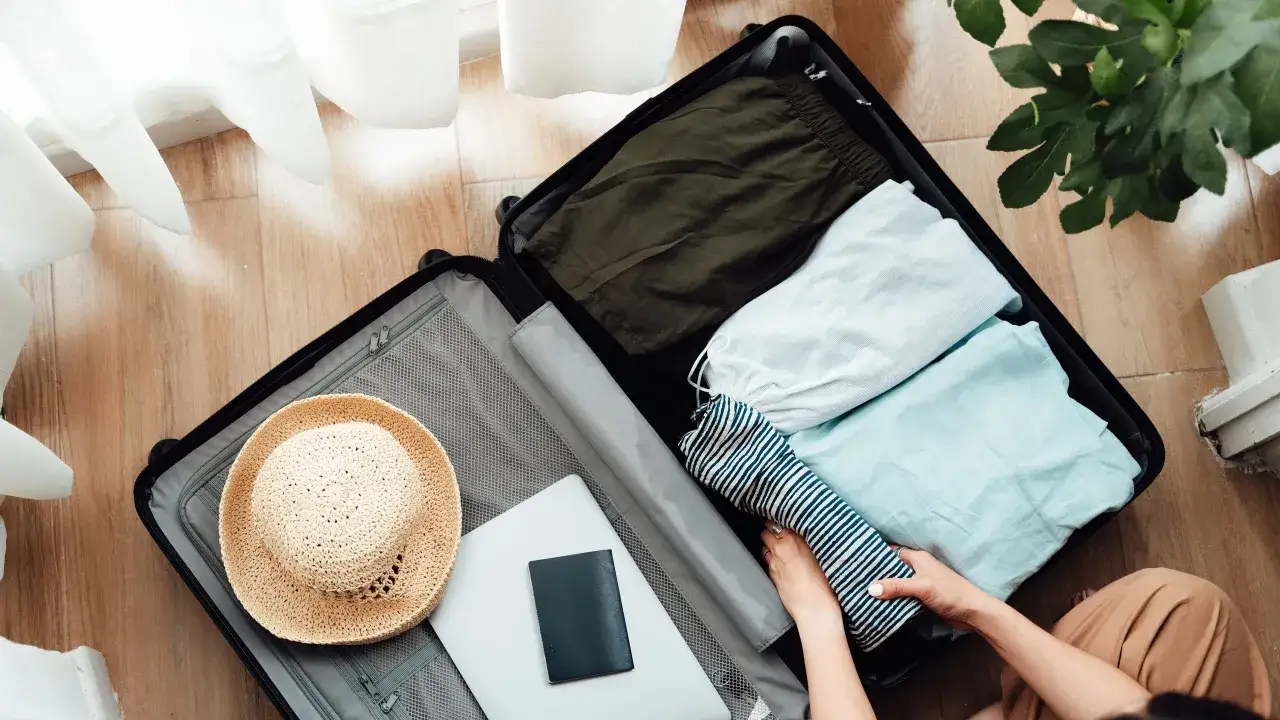 Koffer packen mit cleveren reise hacks: Kleidung, Hut, Laptop und Reisepass liegen bereit.