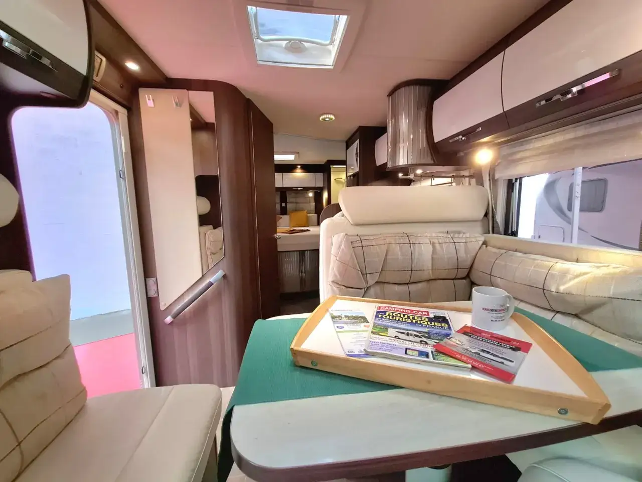 Intérieur d'un camping-car Burstner Fifty Five 55, avec un coin salon confortable, une table garnie de magazines et une tasse.