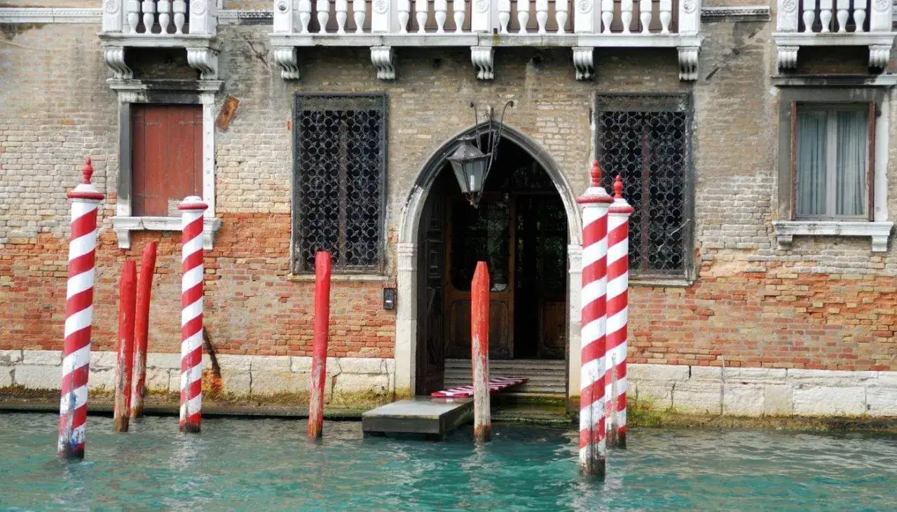 I pali di Venezia, chiamati bricole, segnano il canale davanti a un palazzo storico.