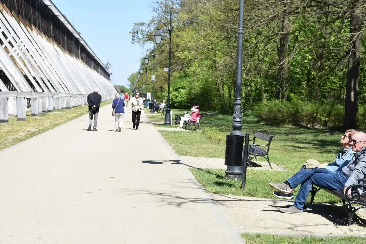 Spacerowicze pod tężniami i w parku, relaksujący się na ławkach. Ciechocinek atrakcje w słoneczny dzień.