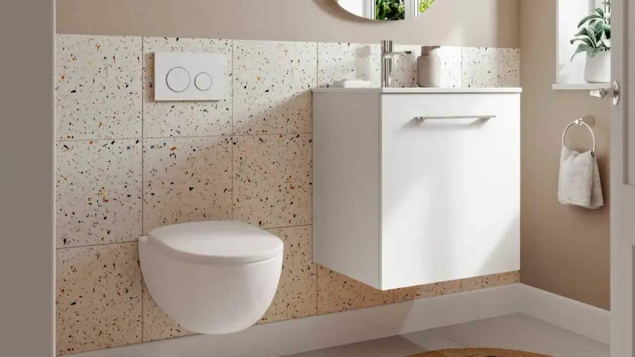 Une toilette suspendue moderne dans une salle de bain aux murs carrelés de terrazzo coloré. Un meuble blanc flottant et un porte-serviettes complètent l'ensemble.