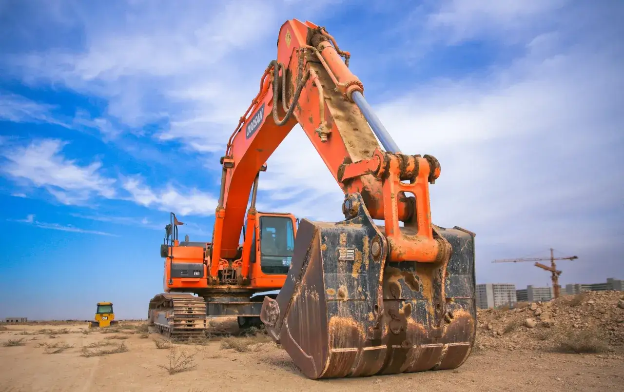 Pomarańczowa minikoparka na placu budowy, gotowa do pracy. Posiadanie uprawnień na minikoparkę otwiera drzwi do wielu możliwości.