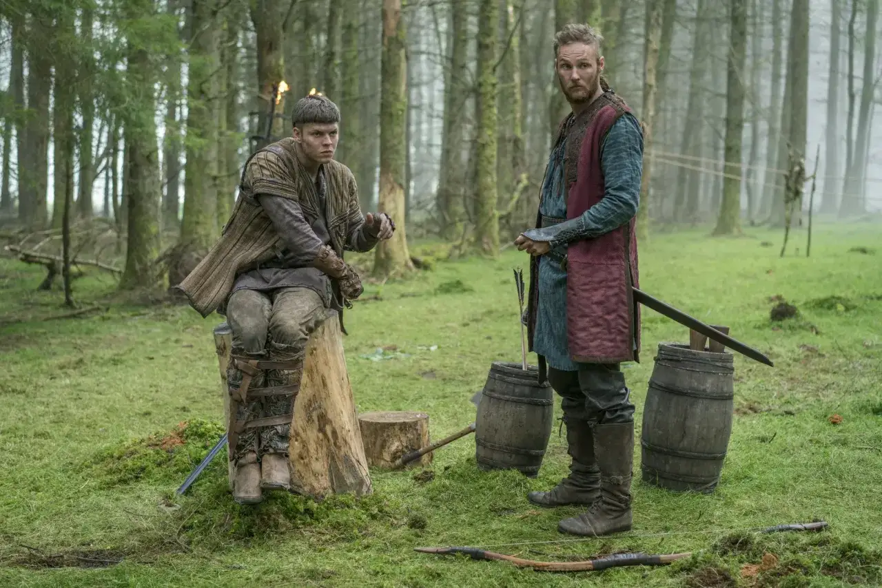 Jordan Patrick Smith jako Ubbe i Alexander Ludwig jako Bjorn w lesie, obok beczek i łuku.