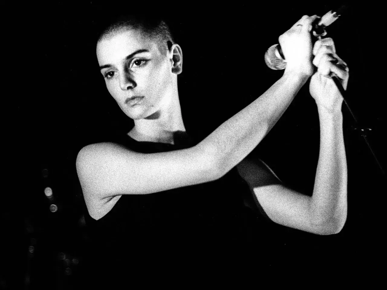 Sinéad O'Connor z mikrofonem, jej wyraz twarzy sugeruje emocjonalne wykonanie jednego z jej niezapomnianych utworów.