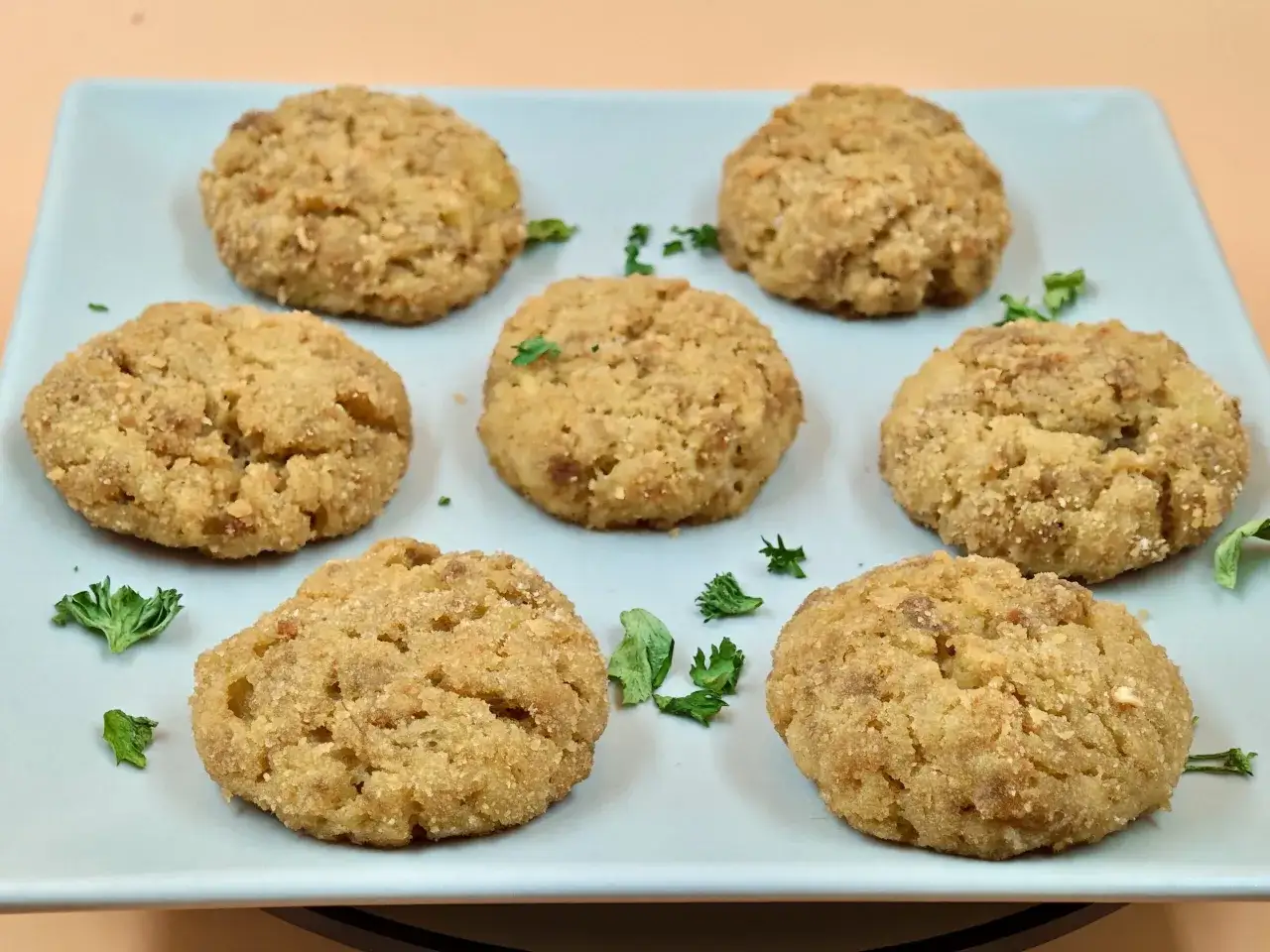 Sei polpette di patate dorate e croccanti, guarnite con prezzemolo fresco, servite su un piatto azzurro.