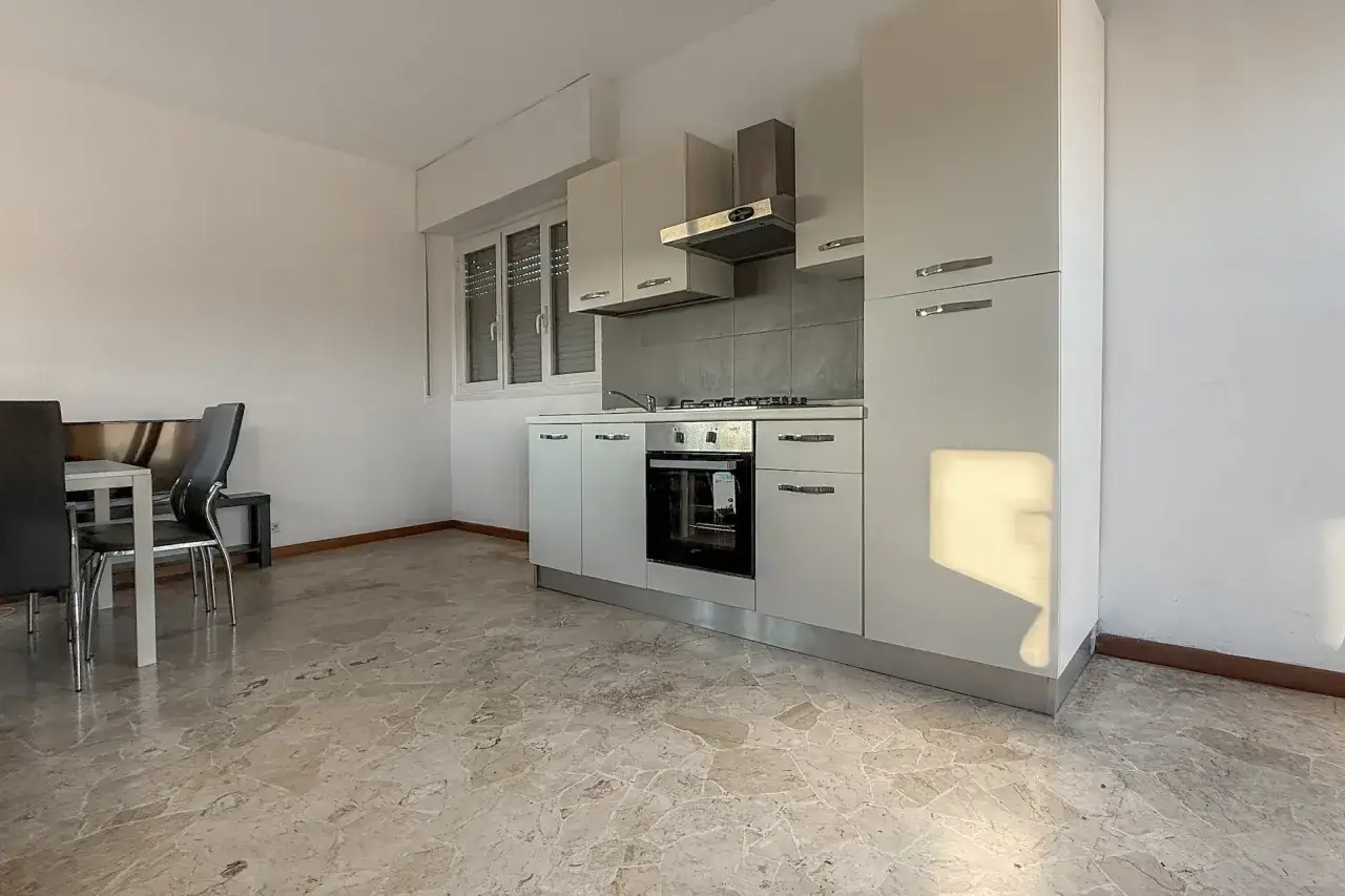 Cucina moderna con piano cottura, forno e pensili bianchi. Tavolo con sedie in primo piano, ideale per un uso foresteria.