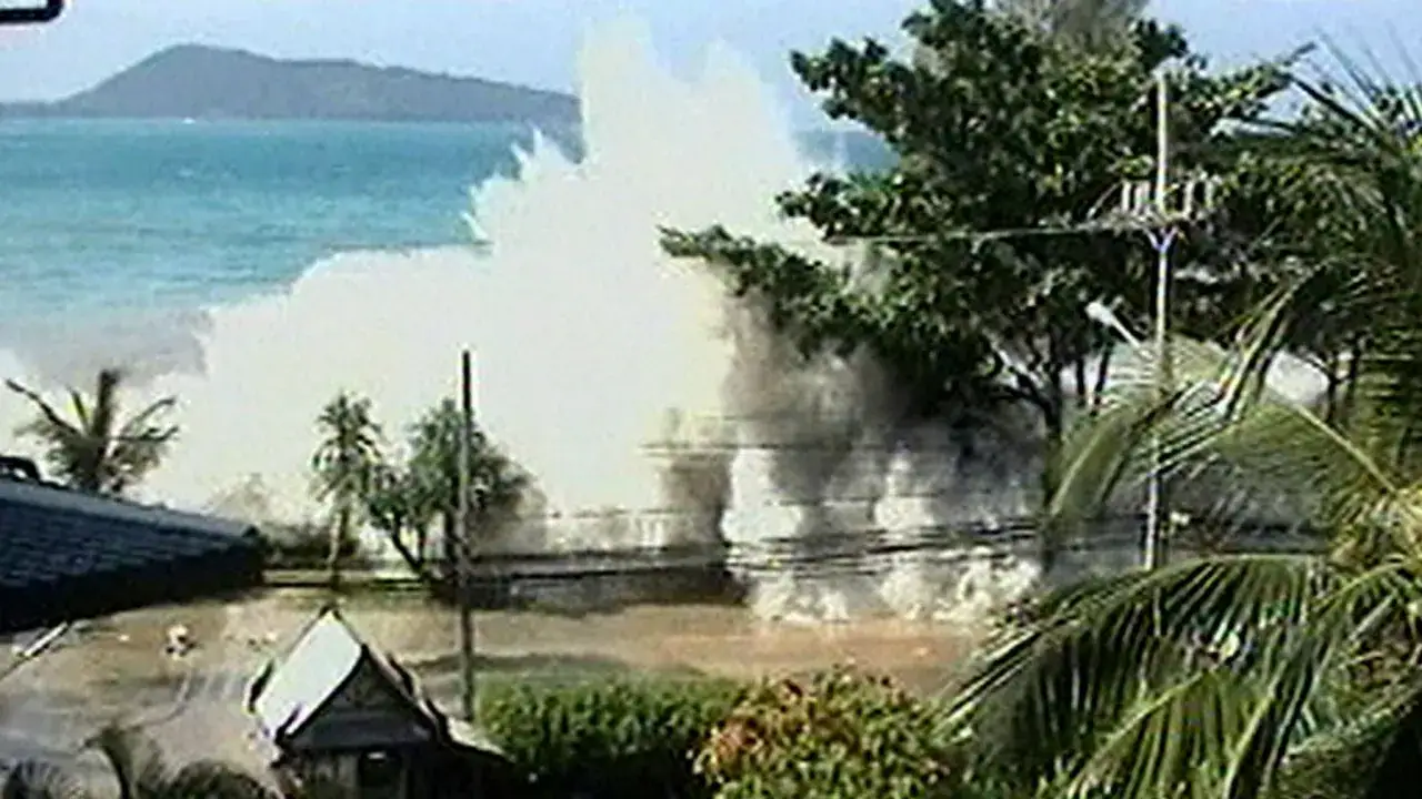 Enorm våg slår in över land, palmer och byggnader. En bild som visar förödelsen efter tsunamin 2004.