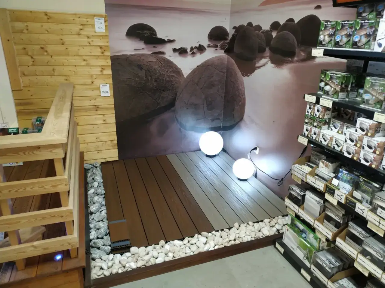 Kompozytowa deska tarasowa w dwóch odcieniach, otoczona kamieniami, z kulistymi lampami.
