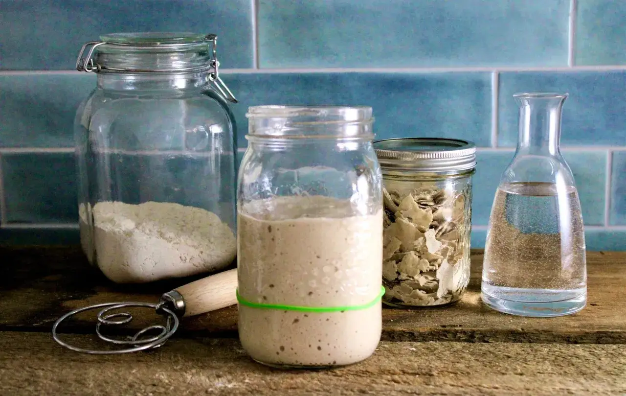 Ingredientes para como hacer masa madre: harina, agua, levadura deshidratada y un batidor.