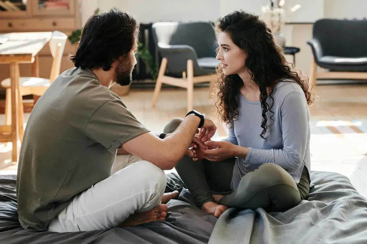 Ein Mann und eine Frau sitzen sich gegenüber und halten Händchen. Sie sprechen leise, was eine tiefe Verbindung und das Wesen einer Beziehung zwischen Mann und Frau zeigt.