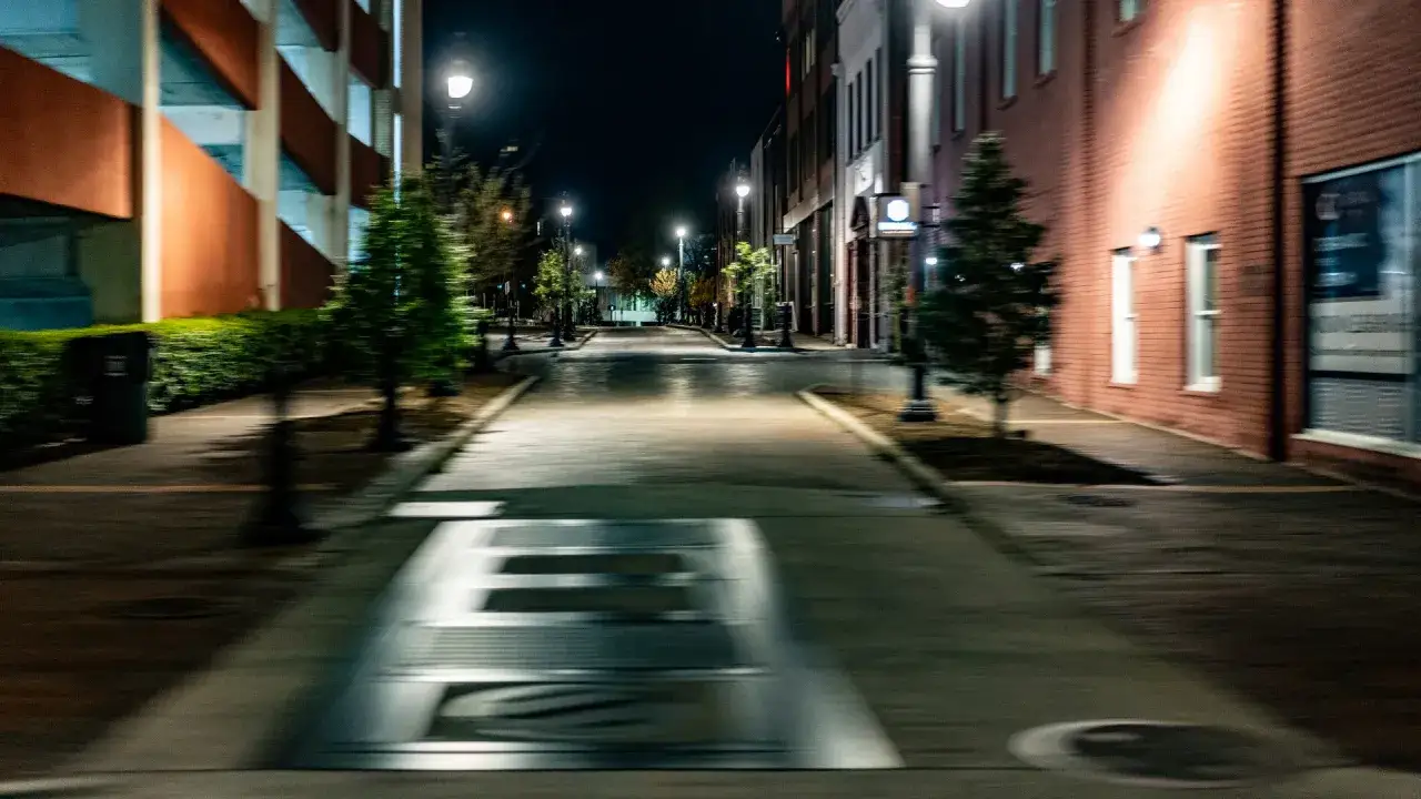 A 40mm street photography capture of a deserted, rain-slicked street at night. Buildings line the path, illuminated by streetlights.