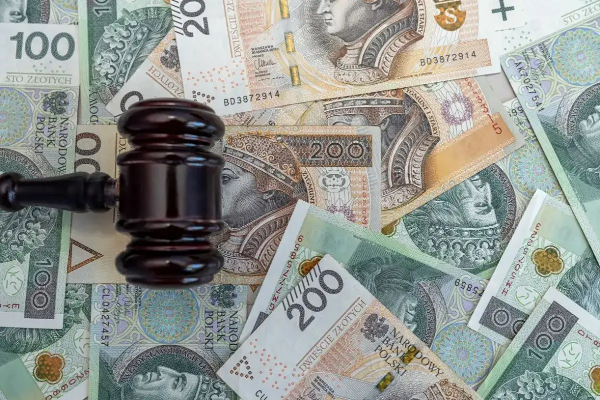 Młotek sędziowski na stosie polskich banknotów symbolizuje odsetki od niezapłaconej faktury i koszty sądowe.