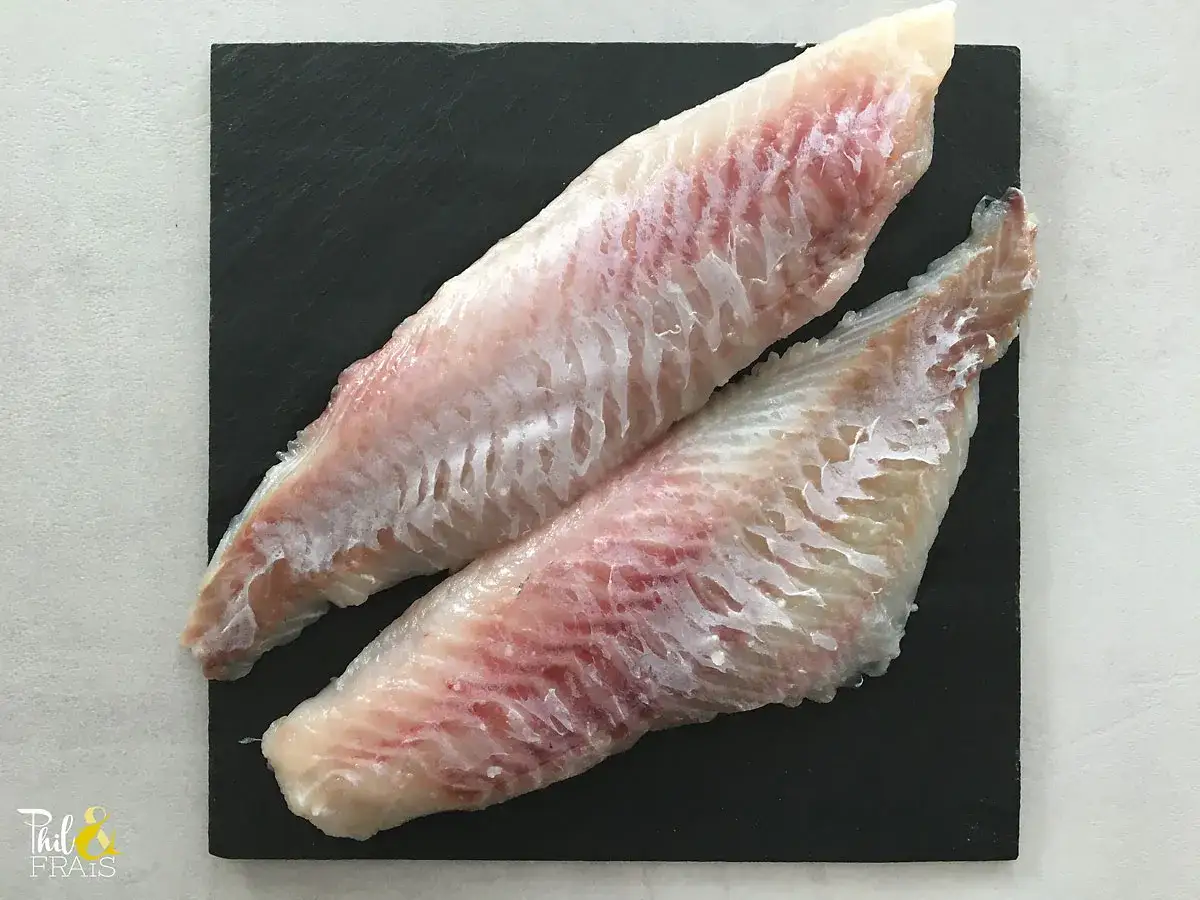 Deux filets de sébaste poisson, d'une chair blanche et rosée, prêts à être cuisinés sur une ardoise noire.