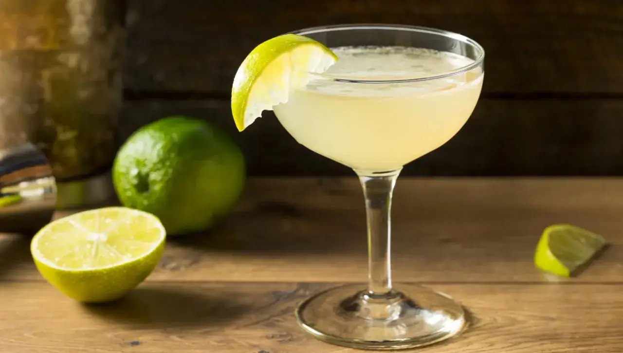Erfrischender Daiquiri Cocktail mit Limettenspalte, daneben ganze und halbe Limetten.
