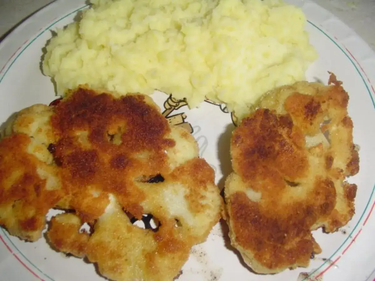 Złociste blumenkohl schnitzel, panierowane i usmażone na chrupko, podane z kremowym purée ziemniaczanym.