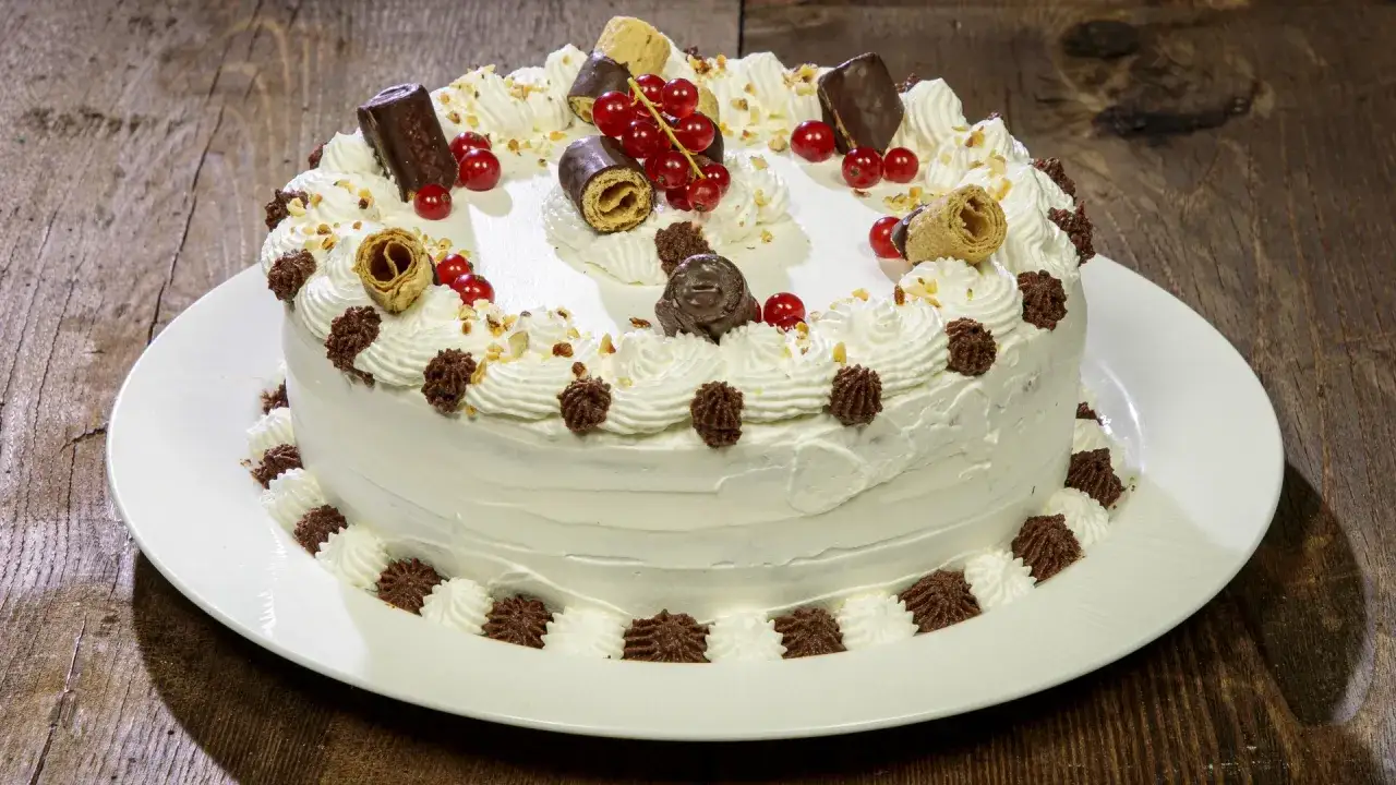 Deliziosa torta compleanno cioccolato e panna, decorata con panna montata, ribes rossi, biscotti e cioccolatini.