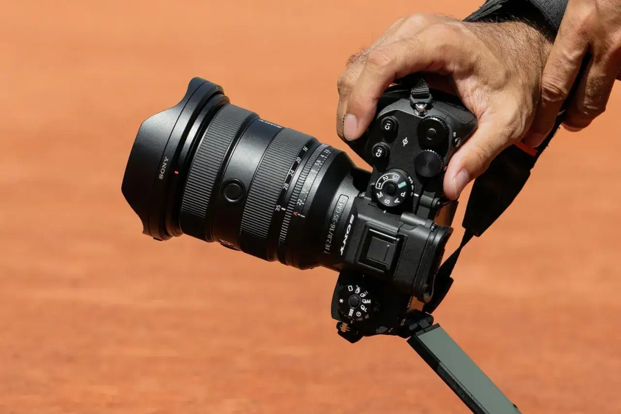 En hand h&aring;ller en Sony a9 III med ett stort objektiv. Kameran &auml;r redo att f&aring;nga &ouml;gonblicket.